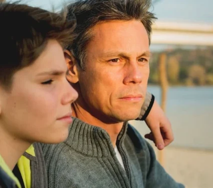 Father-and-his-child-impacted-by-cancer A solemn look on a father and sons face as a result of the impact of cancer